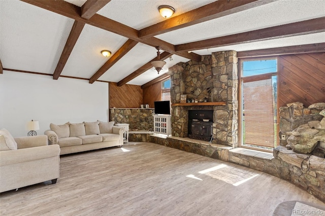 living room featuring light hardwood / wood-style floors, a textured ceiling, wooden walls, vaulted ceiling with beams, and a stone fireplace