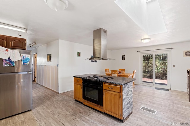 kitchen featuring visible vents, black gas stove, freestanding refrigerator, light wood-style floors, and island range hood