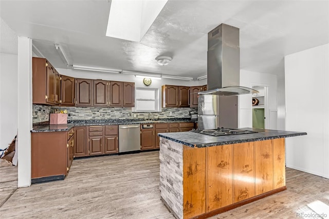 kitchen with light wood-style flooring, appliances with stainless steel finishes, dark countertops, tasteful backsplash, and island range hood