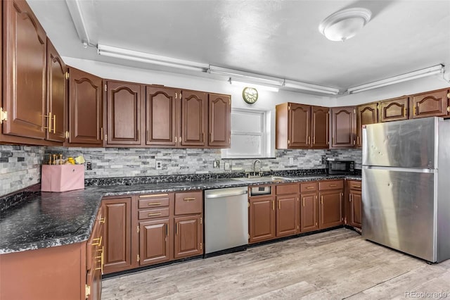 kitchen featuring a sink, stainless steel appliances, dark countertops, and light wood-style flooring