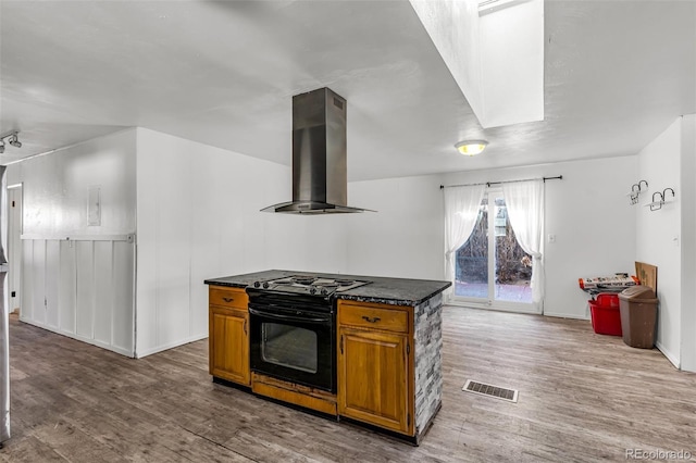 kitchen with ventilation hood, black / electric stove, wood finished floors, brown cabinetry, and visible vents