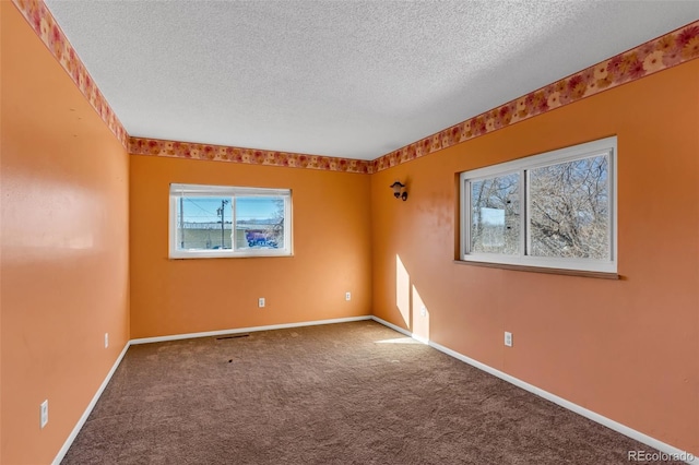 carpeted spare room featuring visible vents, baseboards, and a textured ceiling