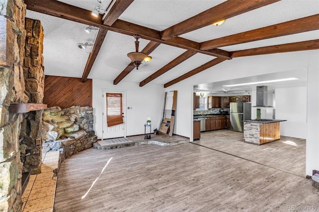 unfurnished living room featuring light wood-style flooring, a textured ceiling, and vaulted ceiling with beams