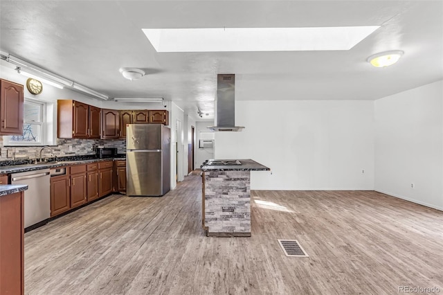 kitchen featuring dark countertops, visible vents, range hood, a skylight, and stainless steel appliances