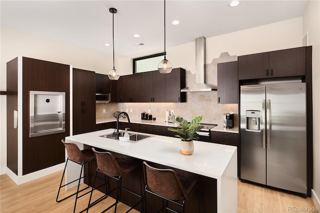 kitchen featuring backsplash, wall chimney range hood, light countertops, appliances with stainless steel finishes, and a sink