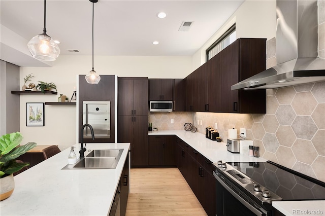 kitchen featuring visible vents, light countertops, stainless steel appliances, wall chimney exhaust hood, and a sink