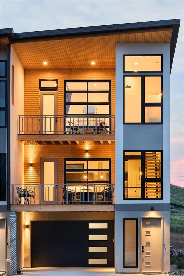 back of property featuring stucco siding, an attached garage, and a balcony