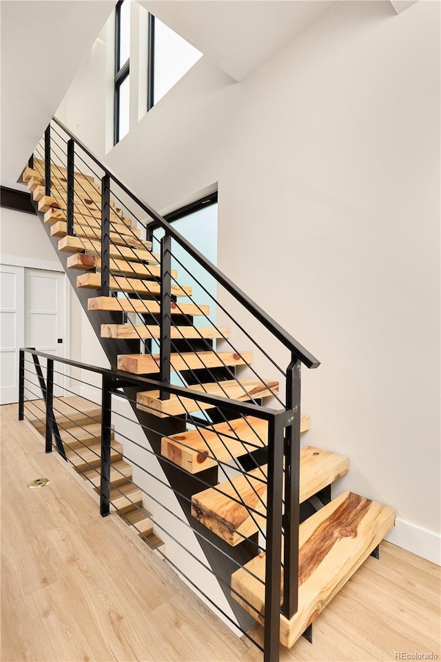 staircase featuring a high ceiling, baseboards, and wood finished floors