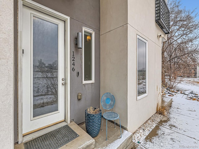 snow covered property entrance with stucco siding