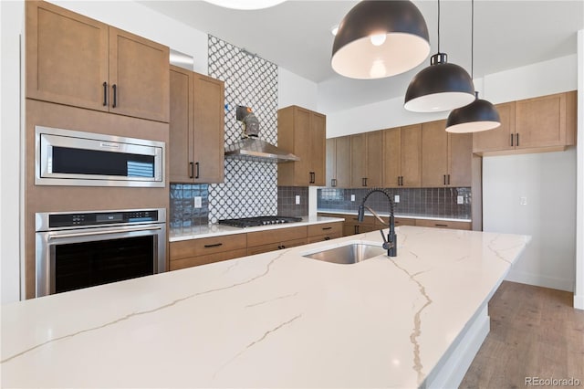 5621 W 141st Ln, Broomfield, CO 80020 - kitchen featuring stainless steel appliances, wall chimney range hood, brown cabinetry, light wood-style floors, and tasteful backsplash