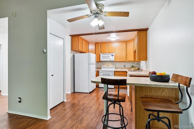 kitchen with a peninsula, wood finished floors, white appliances, a sink, and backsplash