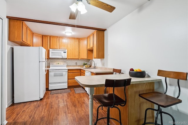 kitchen featuring a kitchen breakfast bar, backsplash, a sink, a peninsula, and white appliances