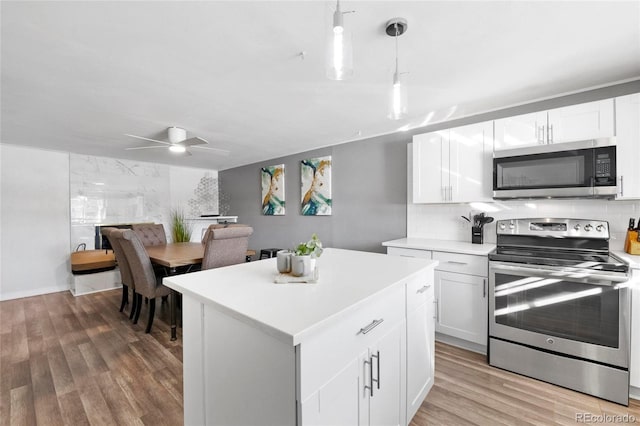 kitchen with light wood-style flooring, a kitchen island, tasteful backsplash, appliances with stainless steel finishes, and light countertops