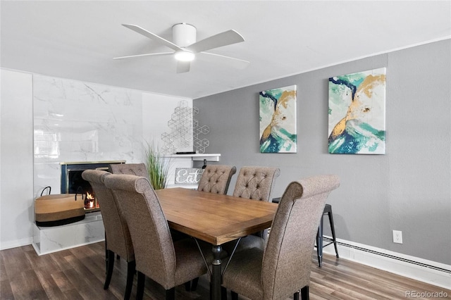 dining room featuring a premium fireplace, wood finished floors, a ceiling fan, and a baseboard radiator