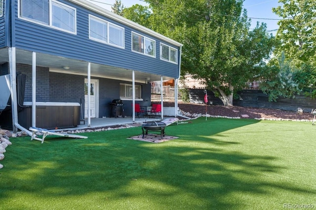 back of property with fence, a yard, a hot tub, a patio area, and brick siding