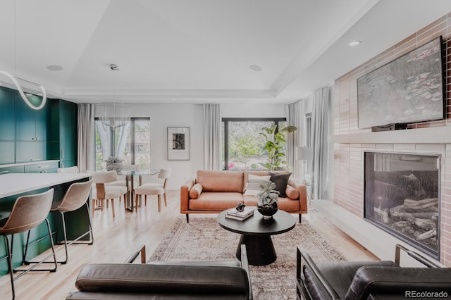 living room with plenty of natural light, a fireplace, a raised ceiling, and light wood-type flooring