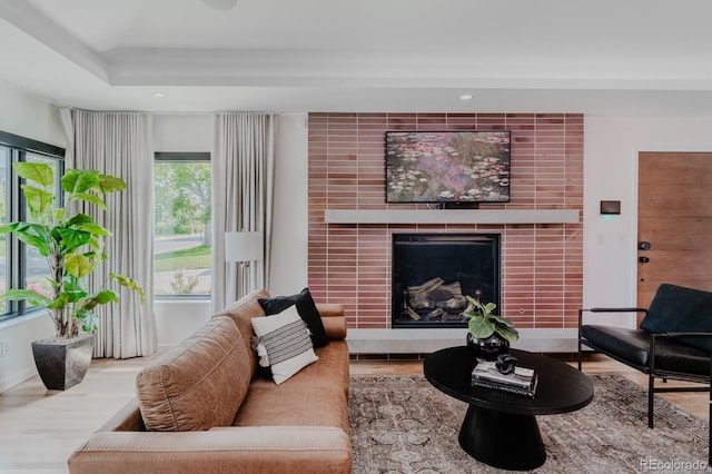 living room featuring hardwood / wood-style floors, a tray ceiling, and a tile fireplace