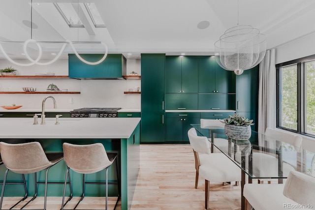 kitchen featuring an island with sink, hanging light fixtures, stove, green cabinetry, and light wood-type flooring