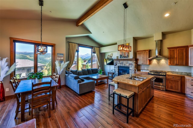 kitchen featuring an island with sink, exhaust hood, stainless steel gas range oven, dark hardwood / wood-style floors, and a fireplace