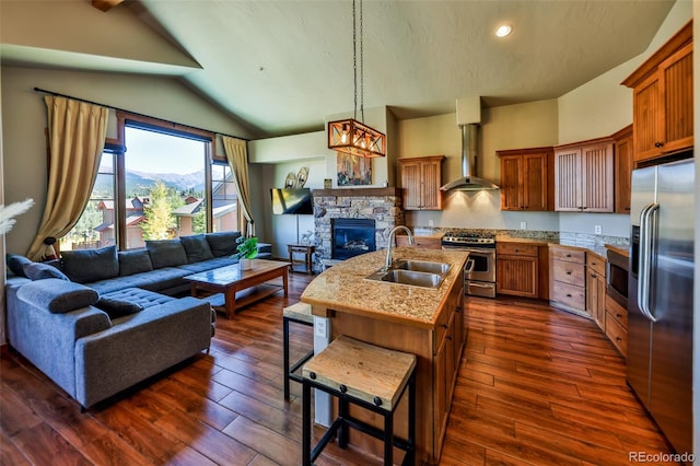 kitchen featuring vaulted ceiling, a fireplace, stainless steel appliances, sink, and wall chimney range hood