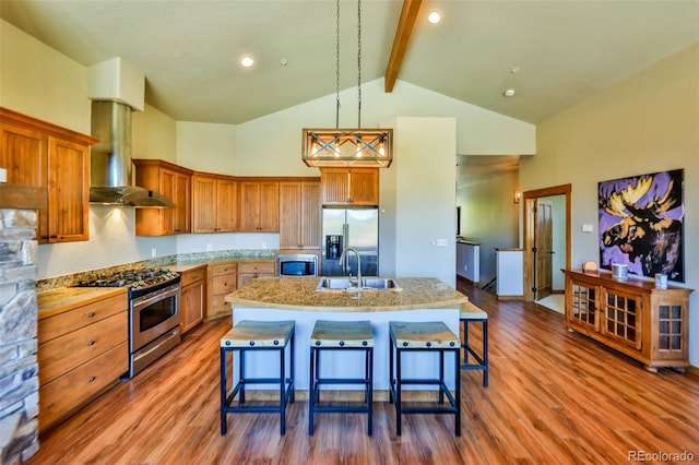 kitchen with beam ceiling, decorative light fixtures, a kitchen island with sink, wall chimney exhaust hood, and stainless steel appliances