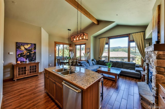 kitchen with a fireplace, pendant lighting, stainless steel dishwasher, a kitchen island with sink, and sink