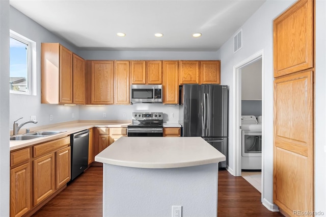 kitchen with appliances with stainless steel finishes, washing machine and dryer, a sink, light countertops, and dark wood-style floors