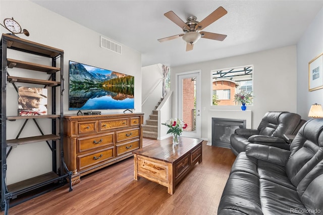 living area with light wood-style flooring, visible vents, ceiling fan, a glass covered fireplace, and stairs