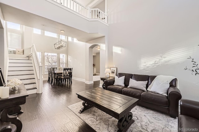 living room featuring stairs, arched walkways, wood finished floors, and a towering ceiling