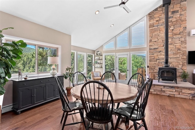 dining room with hardwood / wood-style floors, a baseboard heating unit, ceiling fan, a wood stove, and high vaulted ceiling