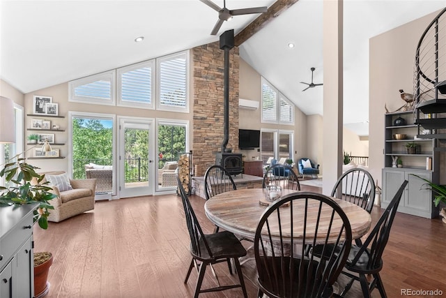 dining room with ceiling fan, a wood stove, hardwood / wood-style flooring, and beamed ceiling