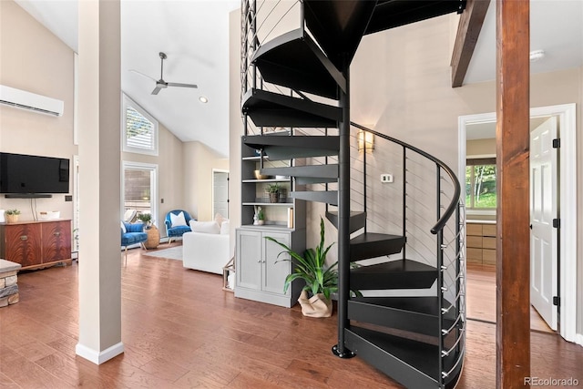 staircase with an AC wall unit, hardwood / wood-style floors, high vaulted ceiling, and ceiling fan