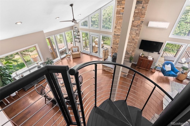 stairs with ceiling fan, wood-type flooring, high vaulted ceiling, and a wall mounted air conditioner