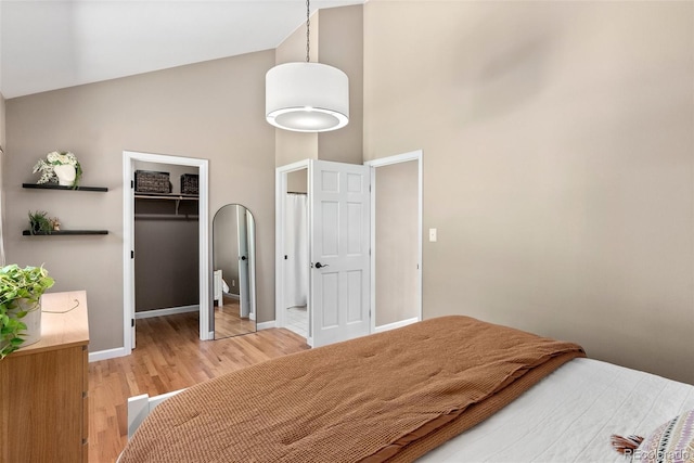 bedroom with light wood-type flooring, a closet, a walk in closet, and high vaulted ceiling