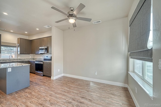 kitchen with ceiling fan, light wood-type flooring, sink, stainless steel appliances, and light stone counters