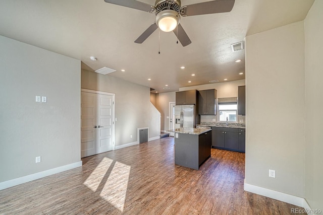 kitchen with stainless steel refrigerator with ice dispenser, sink, light stone counters, a center island, and dark hardwood / wood-style floors