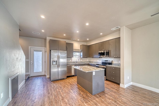 kitchen featuring a center island, stainless steel appliances, sink, light wood-type flooring, and light stone counters