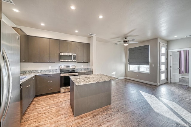 kitchen with light stone countertops, a center island, stainless steel appliances, light wood-type flooring, and ceiling fan