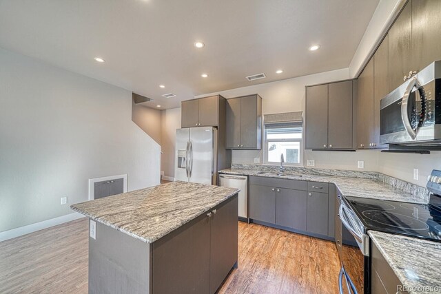 kitchen featuring appliances with stainless steel finishes, a center island, sink, light stone counters, and gray cabinetry