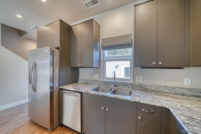 kitchen with appliances with stainless steel finishes, sink, gray cabinets, light wood-type flooring, and light stone counters