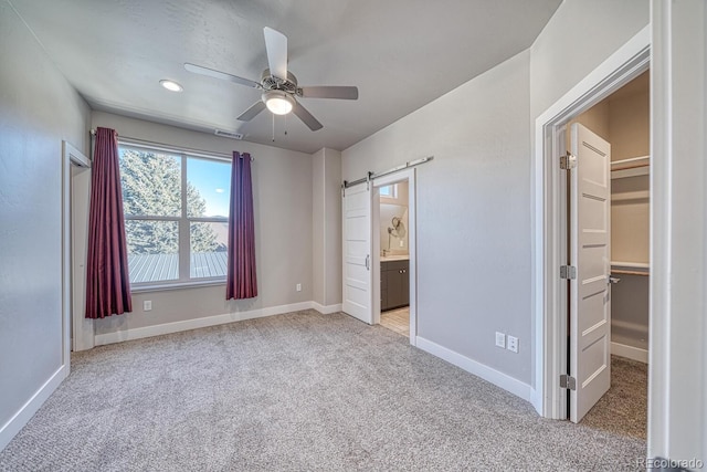 unfurnished bedroom with a walk in closet, light carpet, a closet, ceiling fan, and a barn door