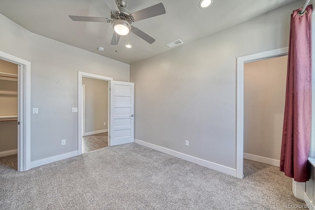 unfurnished bedroom featuring ceiling fan, a closet, a spacious closet, and light carpet