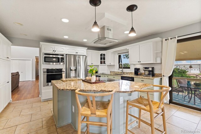 kitchen with appliances with stainless steel finishes, white cabinetry, light stone counters, light wood-type flooring, and a kitchen island