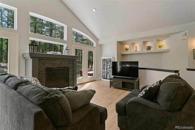 living room featuring high vaulted ceiling, a stone fireplace, and light wood-type flooring