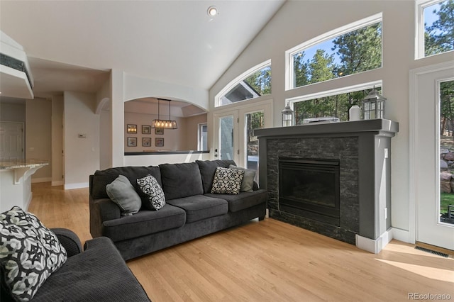 living room featuring a stone fireplace, high vaulted ceiling, plenty of natural light, and light wood-type flooring