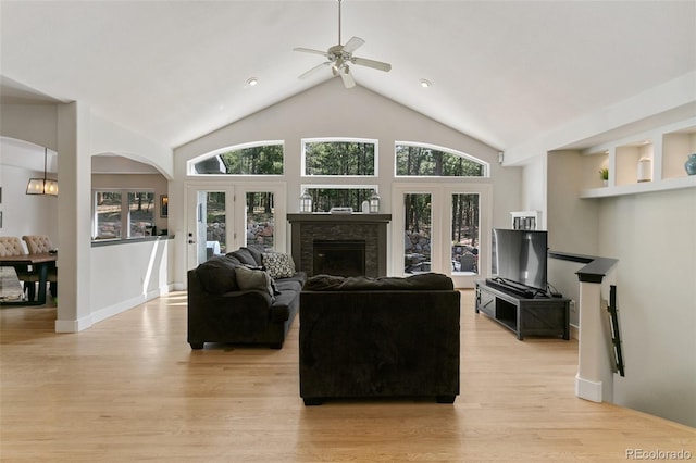 living room featuring a fireplace, ceiling fan, light wood-type flooring, high vaulted ceiling, and french doors