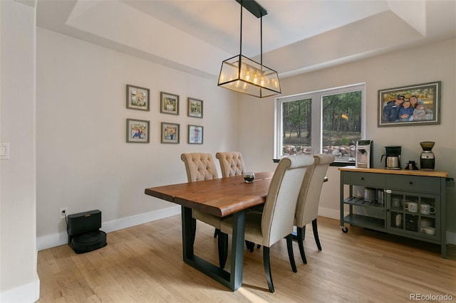 dining area featuring a chandelier, a raised ceiling, and light hardwood / wood-style flooring