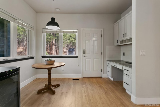 kitchen featuring light hardwood / wood-style floors, light stone counters, backsplash, hanging light fixtures, and white cabinets