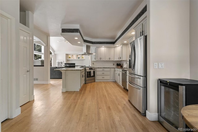 kitchen with light hardwood / wood-style floors, beverage cooler, a kitchen bar, wall chimney exhaust hood, and appliances with stainless steel finishes