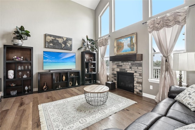 living room with hardwood / wood-style flooring, a wealth of natural light, a high ceiling, and a stone fireplace